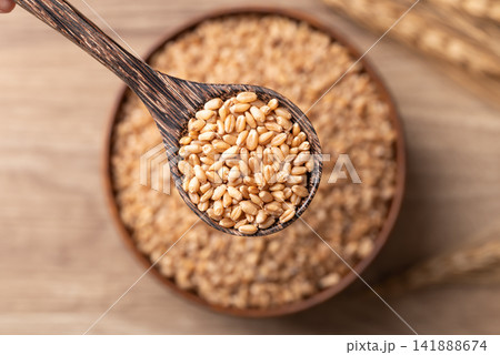 Close-up of whole wheat grain in a wooden spoon, Food ingredients, Top view 141888674