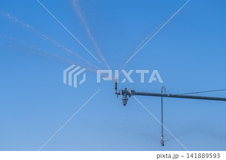 Water sprayers glistening under the bright blue sky during warm afternoon in a lush green field Water sprayers glistening under the bright blue sky during warm afternoon in a lush green field 141889593
