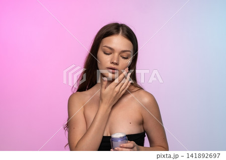 Woman applying cream to her face, eyes closed, maintaining beauty and healthy skincare routine Woman applying cream to her face, eyes closed, maintaining beauty and healthy skincare routine 141892697