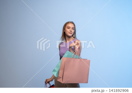 Young woman enjoying retail therapy, carrying colorful shopping bags after successful purchase on blue background 141892906