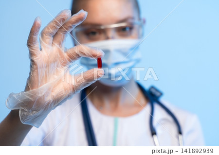 Healthcare professional wearing protective gear holding red pill, representing medical treatment and drug development concept Healthcare professional wearing protective gear holding red pill, representing medical treatment and drug development concept 141892939