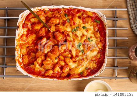 Baked gnocchi with tomato sauce, cheese and basil in casserole dish with serving spoon Baked gnocchi with tomato sauce, cheese and basil in casserole dish with serving spoon 141893155