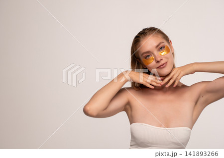 Young woman applying golden eye patches for skincare and beauty routine, getting facial treatment for healthy skin Young woman applying golden eye patches for skincare and beauty routine, getting facial treatment for healthy skin 141893266