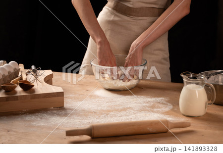 Hands mixing dough in a bowl, preparing ingredients for baking homemade pastry on a rustic wooden table Hands mixing dough in a bowl, preparing ingredients for baking homemade pastry on a rustic wooden table 141893328