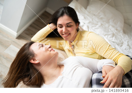 Two women relaxing together on a cozy bed in a warmly lit home interior. Friendship sisterhood family bonding and emotional support between women Two women relaxing together on a cozy bed in a warmly lit home interior. Friendship sisterhood family bonding and emotional support between women 141893416