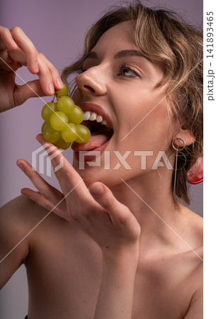 Young woman enjoying fresh green grapes, symbolizing healthy eating, natural beauty, and a joyful lifestyle 141893465