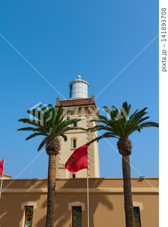 Lighthouse tower with Moroccan flag and palm trees in Tangier under clear blue sky Lighthouse tower with Moroccan flag and palm trees in Tangier under clear blue sky 141893708