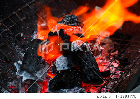 Close-up of burning charcoal with bright orange flames in a barbecue grill. Close-up of burning charcoal with bright orange flames in a barbecue grill. 141893779