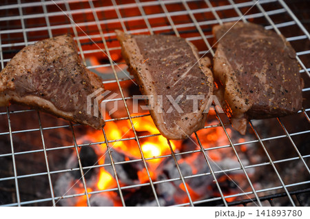 Grilled beef steak cooking on a charcoal fire. BBQ moments that bring people together. Grilled beef steak cooking on a charcoal fire. BBQ moments that bring people together. 141893780