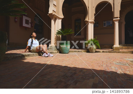 Woman relaxing in sunlit Tangier courtyard with backpack and Moorish arches Woman relaxing in sunlit Tangier courtyard with backpack and Moorish arches 141893786
