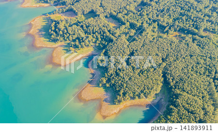 Top down aerial view of bright turquoise water of Lake Plastiras meeting dense green forest along jagged shoreline in Greece 141893911