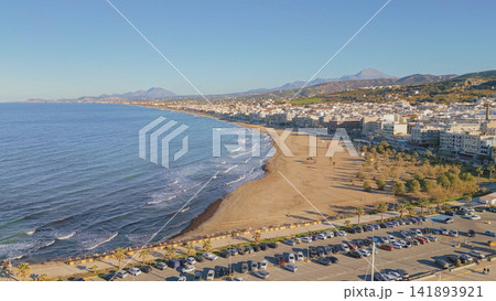 Aerial view of sandy city beach and Mediterranean coastline in Rethymno town with Crete mountain landscape and clear blue sky in background Greece Aerial view of sandy city beach and Mediterranean coastline in Rethymno town with Crete mountain landscape and clear blue sky in background Greece 141893921