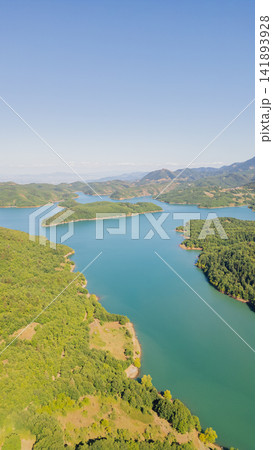 Vertical aerial view of Plastiras Lake surrounded by green forest hills and mountains under clear blue sky on sunny summer day in Karditsa Greece Vertical aerial view of Plastiras Lake surrounded by green forest hills and mountains under clear blue sky on sunny summer day in Karditsa Greece 141893928