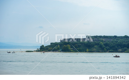 Medieval fortress rising above a green island surrounded by Lake Garda in northern Italy. Concept of history, travel, nature and cultural heritage Medieval fortress rising above a green island surrounded by Lake Garda in northern Italy. Concept of history, travel, nature and cultural heritage 141894342