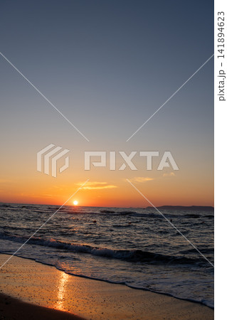 Bright orange sunset over dark ocean waves with reflection on wet shore 141894623