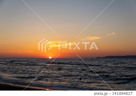 Vibrant orange sunset over ocean waves with distant island silhouette Vibrant orange sunset over ocean waves with distant island silhouette 141894627