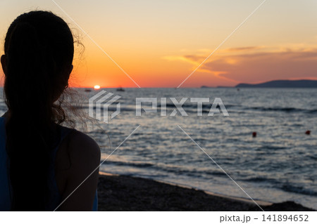 Silhouette of young woman looking at golden sunset over ocean waves 141894652