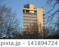 Tall brutalist high-rise building with large windows and cellular antennas against a clear blue sky. Modernist urban architecture, office skyscraper, city development, and real estate concept. 141894724