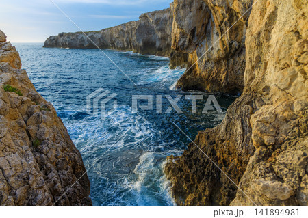 Rugged coastal cliffs meet the deep blue sea with crashing waves Rugged coastal cliffs meet the deep blue sea with crashing waves 141894981