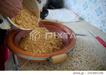Authentic Moroccan couscous being prepared in a clay tagine by a woman pouring semolina Authentic Moroccan couscous being prepared in a clay tagine by a woman pouring semolina 141895146