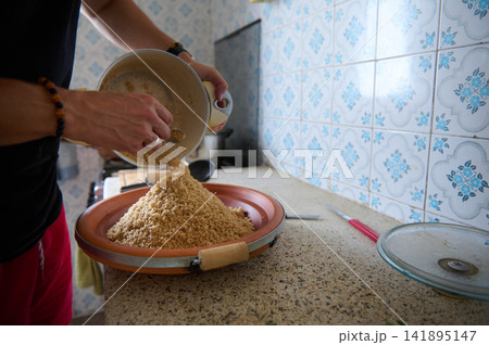 Preparing authentic Moroccan couscous in a home kitchen with hands pouring semolina into a plate 141895147