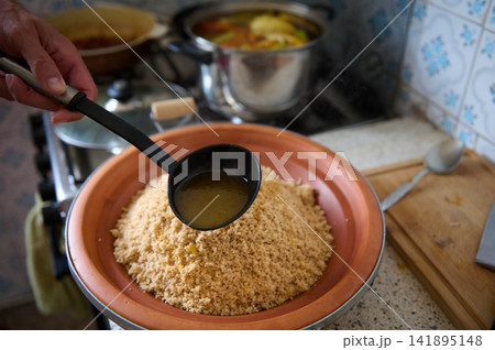Authentic Moroccan couscous with vegetables being ladled with broth in a home kitchen Authentic Moroccan couscous with vegetables being ladled with broth in a home kitchen 141895148