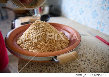 Authentic Moroccan couscous dish on a clay plate in a home kitchen preparing semolina grain Authentic Moroccan couscous dish on a clay plate in a home kitchen preparing semolina grain 141895157