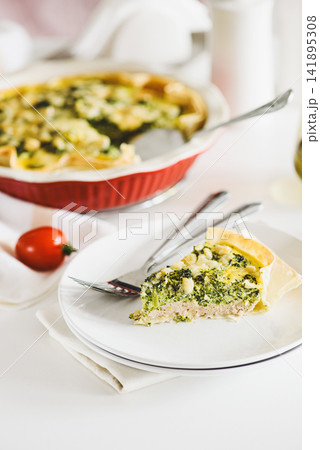 Freshly Baked Broccoli Quiche Slice on a Plate with Whole Quiche Background and Tomato Freshly Baked Broccoli Quiche Slice on a Plate with Whole Quiche Background and Tomato 141895308