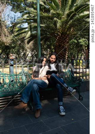 Couple reading book together in park sitting on bench Couple reading book together in park sitting on bench 141895467