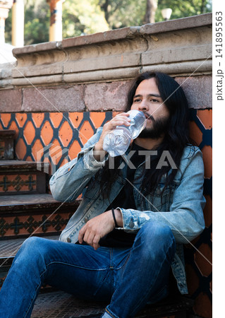 Man drinking water bottle sitting on stairs Man drinking water bottle sitting on stairs 141895563