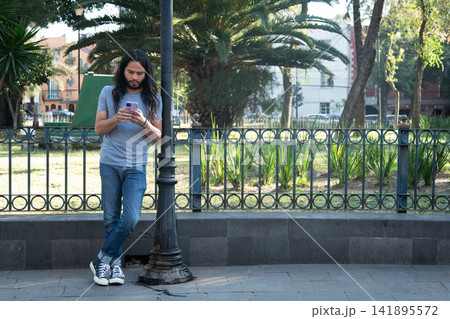 Man with long hair using phone in urban park Man with long hair using phone in urban park 141895572