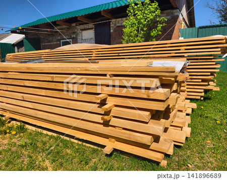 Wood timber planks stacked outdoors on green grass, ready for building a new house or renovation, illuminated by bright sunlight on a clear day. Wood timber planks stacked outdoors on green grass, ready for building a new house or renovation, illuminated by bright sunlight on a clear day. 141896689