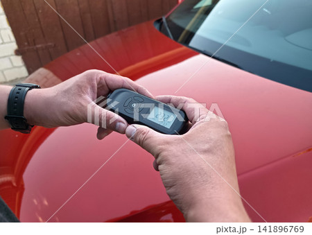 Hands holding digital paint thickness gauge with reading over red car hood. Used car inspection, pre-purchase check, accident and repaint detection, auto appraisal concept. 141896769