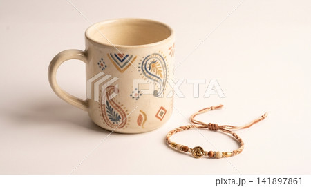 Ceramic mug with paisley patterns next to a wooden beaded bracelet drinkware accessory handmade bohemian textured minimalist composition background creative adornment decoration Ceramic mug with paisley patterns next to a wooden beaded bracelet drinkware accessory handmade bohemian textured minimalist composition background creative adornment decoration 141897861