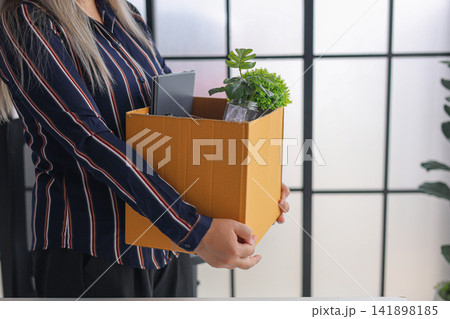 Businesswoman Carrying Cardboard Box with Personal Belonging in Office Businesswoman Carrying Cardboard Box with Personal Belonging in Office 141898185