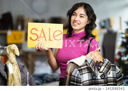 Happy female shopper holds a sign saying Sale in clothing store Happy female shopper holds a sign saying Sale in clothing store 141898541