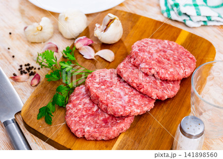 Formed raw burgers of pork and beef on a chopping board next to a whole garlic and parsley in the restaurant kitchen Formed raw burgers of pork and beef on a chopping board next to a whole garlic and parsley in the restaurant kitchen 141898560