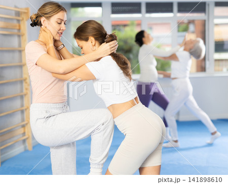 Young woman performing knee strike in midsection to female opponent during self-defense course Young woman performing knee strike in midsection to female opponent during self-defense course 141898610