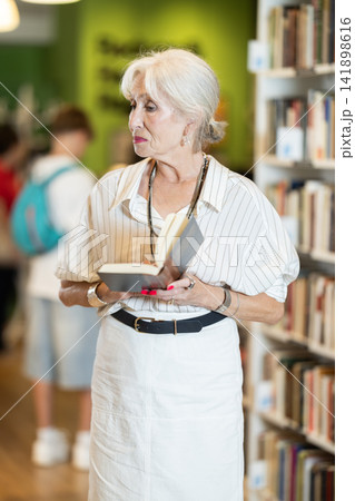 Elderly woman choosing book in bookstore Elderly woman choosing book in bookstore 141898616