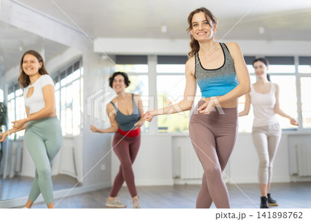 Happy women dancing synchronous group choreography in dance hall Happy women dancing synchronous group choreography in dance hall 141898762