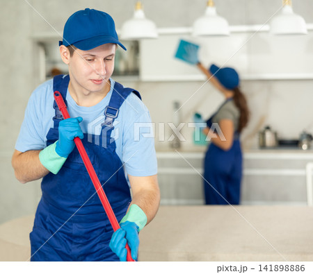 Young boy in blue uniform cleaning the floor in the kitchen Young boy in blue uniform cleaning the floor in the kitchen 141898886