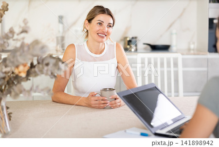 Woman talks to anb agent while sitting at table in kitchen Woman talks to anb agent while sitting at table in kitchen 141898942