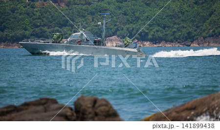Naval patrol boat cruising through coastal waters on a sunny day against a lush green mountain backdrop Naval patrol boat cruising through coastal waters on a sunny day against a lush green mountain backdrop 141899438