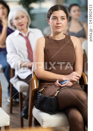 Young woman sitting on chair and listening to presentation Young woman sitting on chair and listening to presentation 141902413