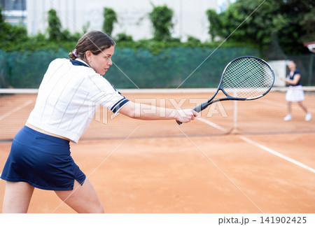 Girl plays tennis on open court with opponent 141902425