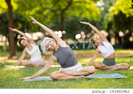 Elderly woman stretching in lotus position at outdoor yoga class Elderly woman stretching in lotus position at outdoor yoga class 141902462
