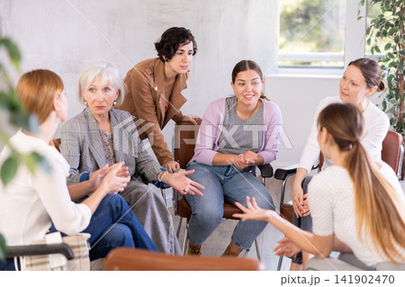 Friendly group of women discussing sitting on chairs in circle Friendly group of women discussing sitting on chairs in circle 141902470