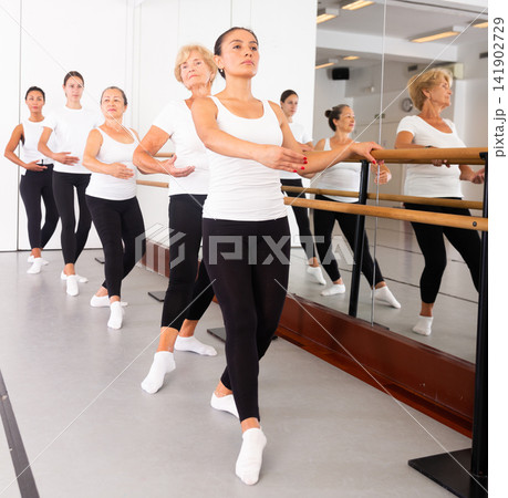 Group of women engaged in ballet in a dance studio performs a choreographic exercise 141902729