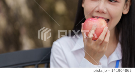 Asian woman biting into fresh red apple outdoors for healthy nutrition and dental care 141904865