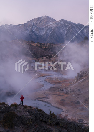 Solitary hiker admires steam over hot spring valley near sierra nevada mountain range feeling peaceful wonder during serene dawn Solitary hiker admires steam over hot spring valley near sierra nevada mountain range feeling peaceful wonder during serene dawn 141905916